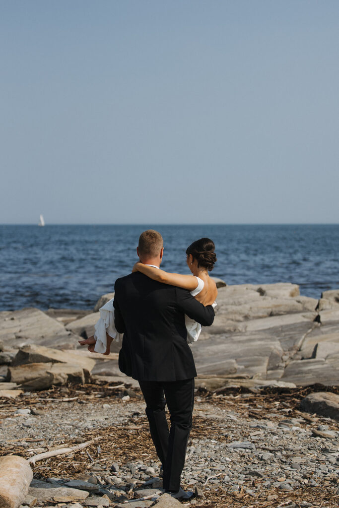 Groom carrying bride on the rocks by the ocean in new hampshire