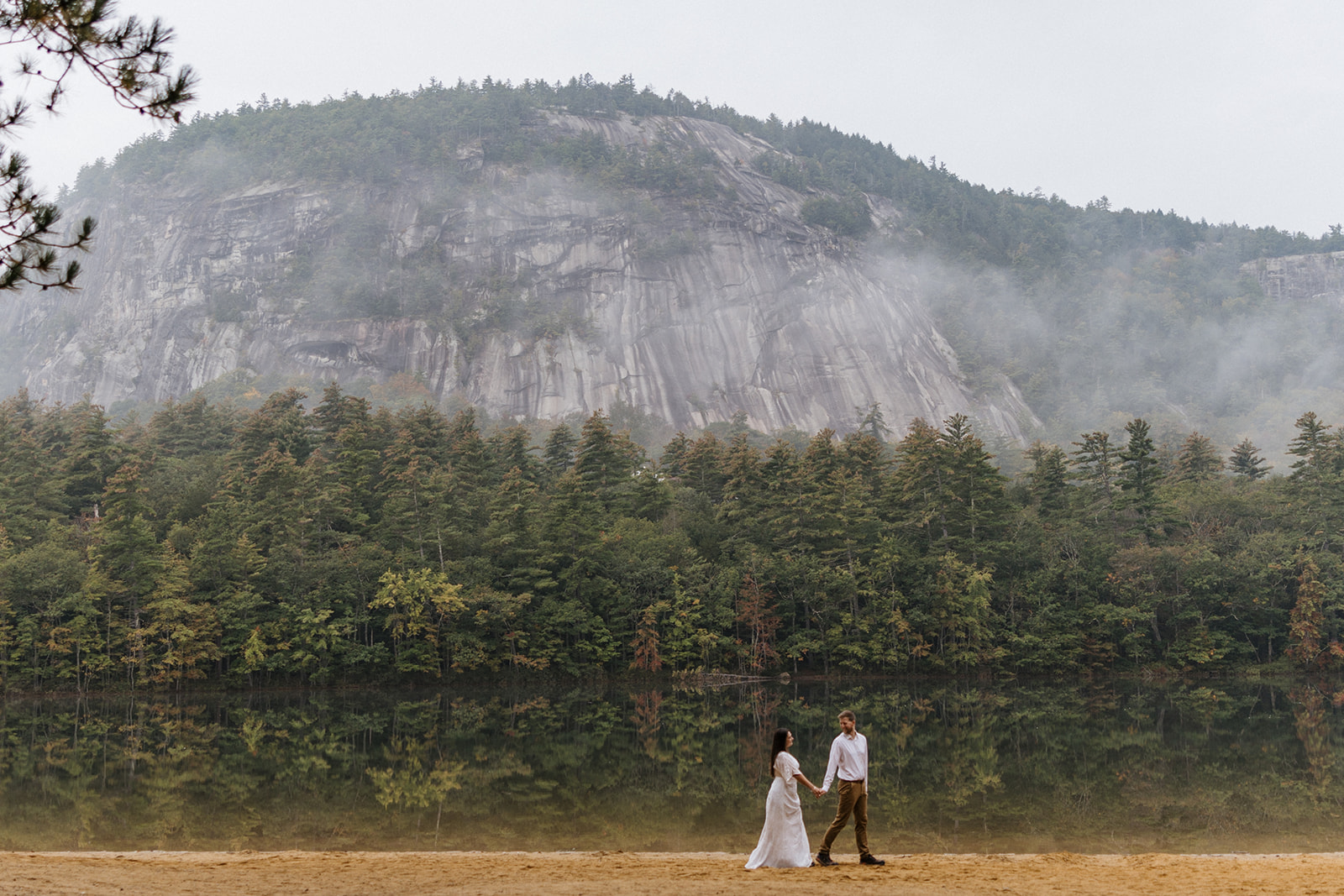 stunning couple walk by a NH lake with a mountain in the background
