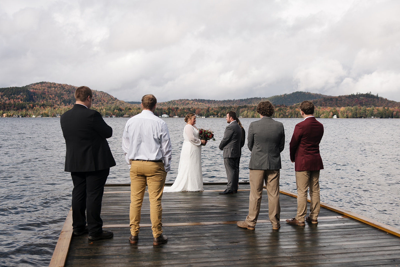 bride and groom surrounded by friends and family on a lake dock say I do