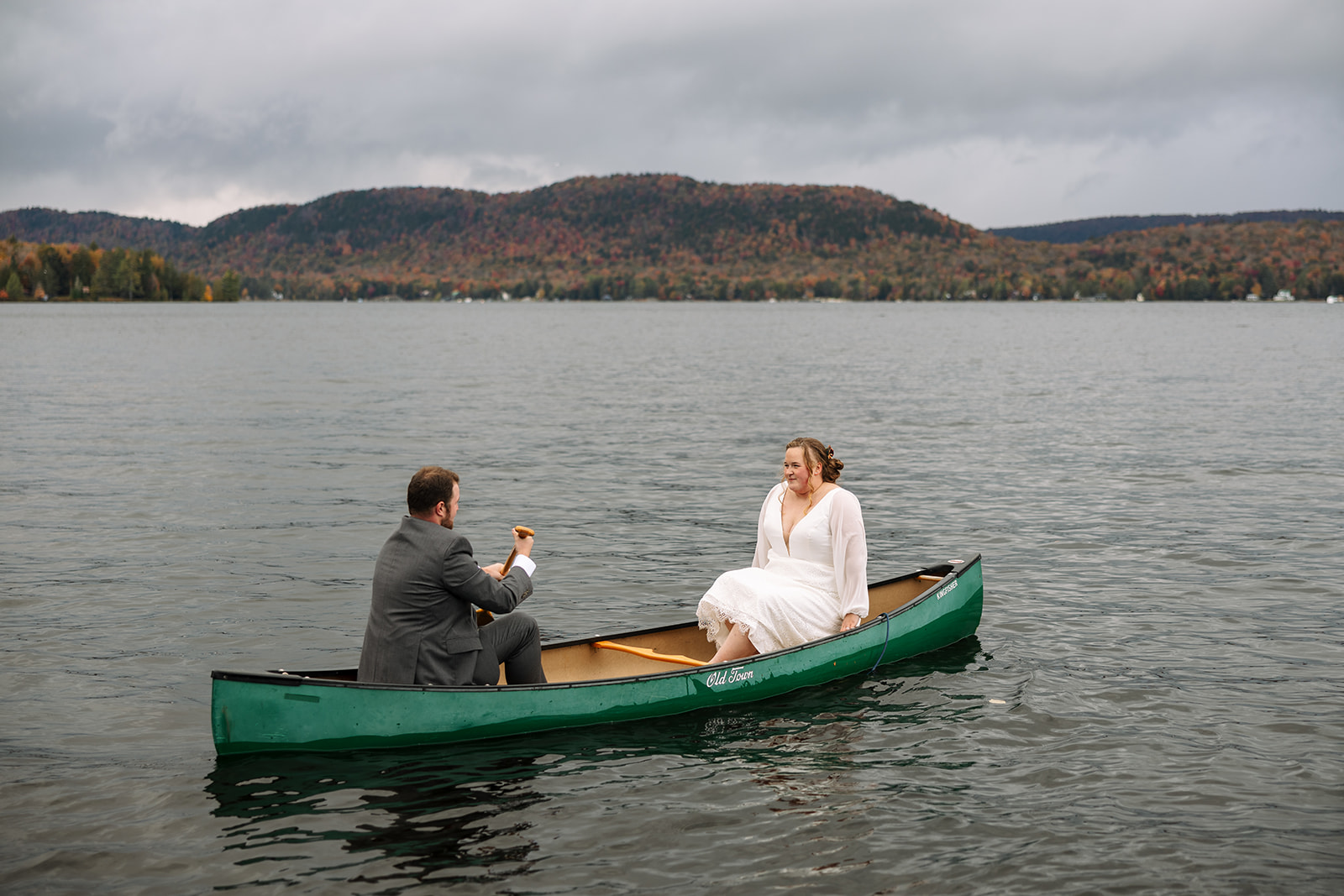 bride and groom row in a canoe after their upstate NY wedding ceremony