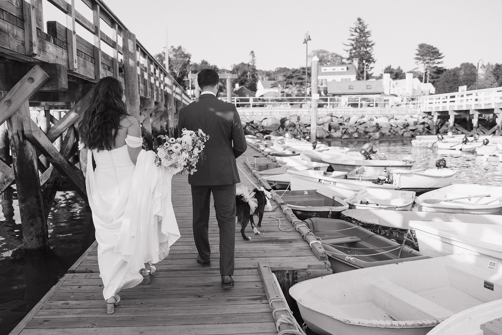 Bride and groom walking with their dog on the docks at Pepperrell Cove in Kittery, Maine