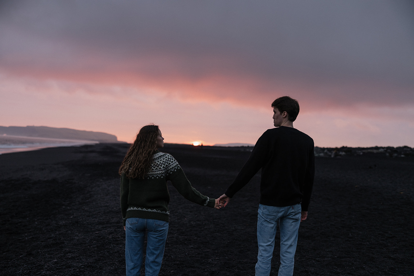 stunning couple walk on the icelandic beach at sunset