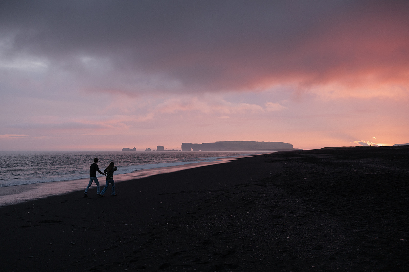 stunning couple walk on the icelandic beach at sunset