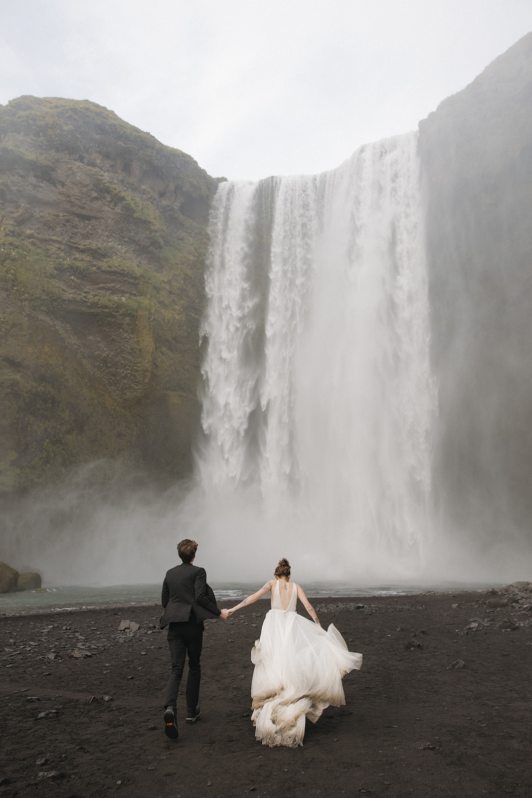 Bride and groom at the bottom of Skogafoss waterfall during their Iceland elopement