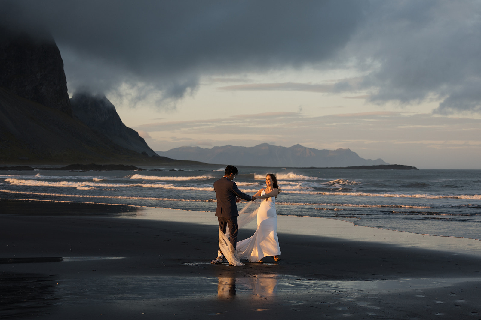 bride and groom hold hands on the black sand beach during sunset while in iceland