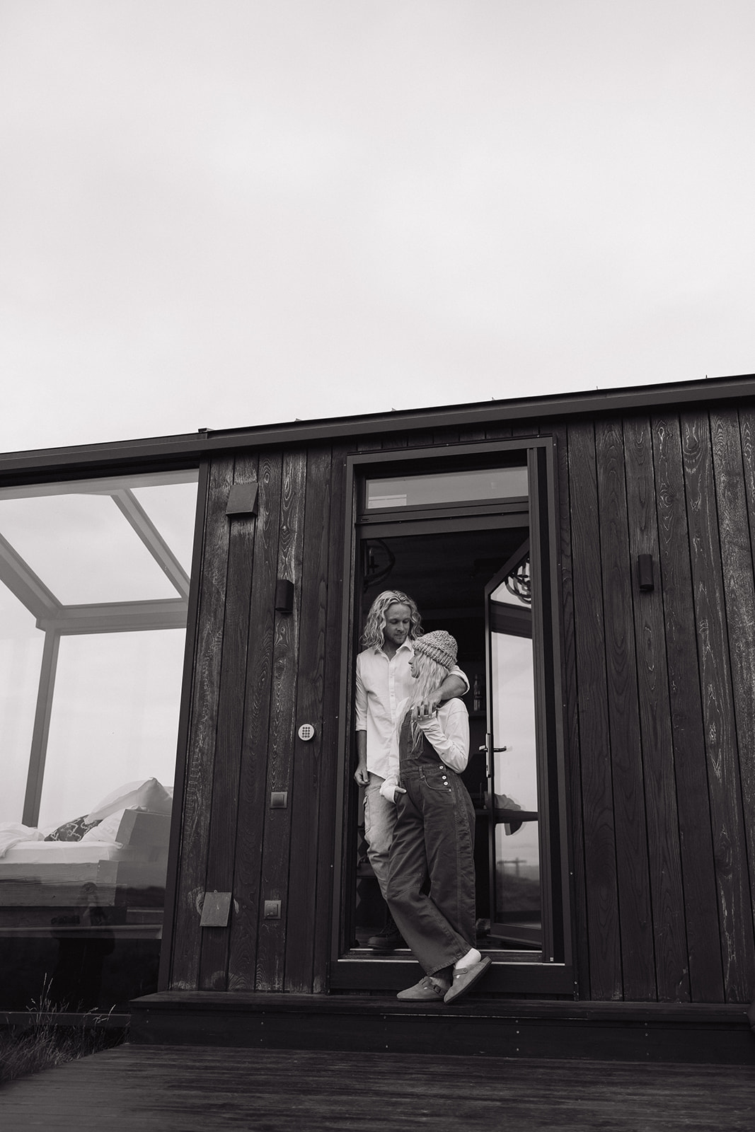 bride and groom lean against the side door of their glass house in iceland