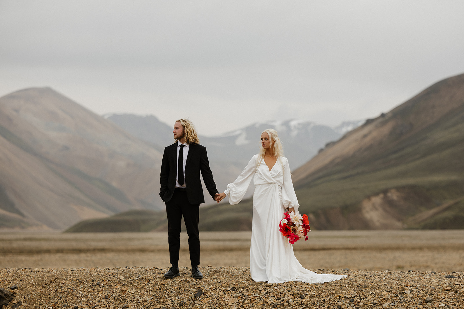 bride and groom pose in iceland while holding bright red bridal florals