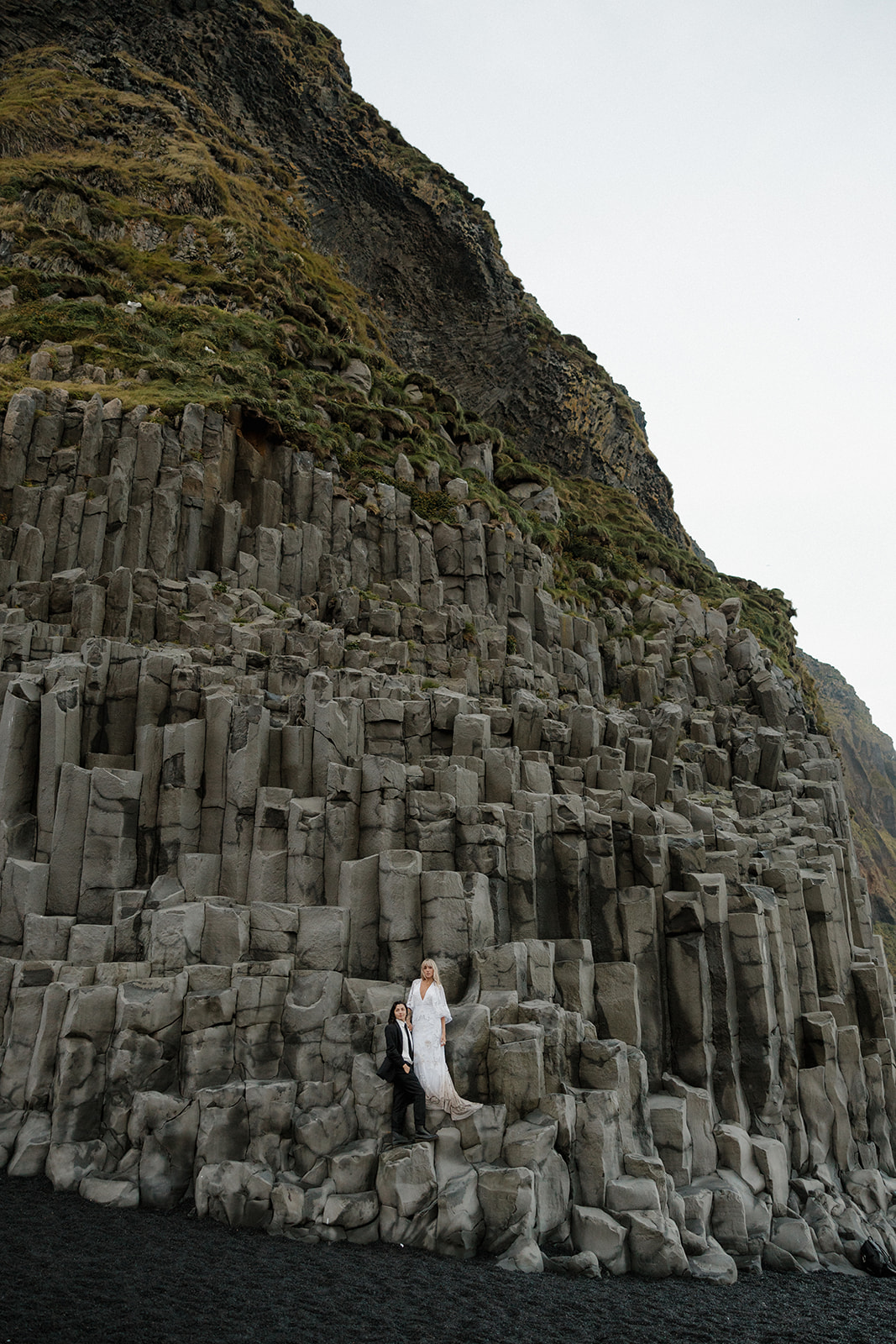 same sex couple pose on a rocky cliff in iceland