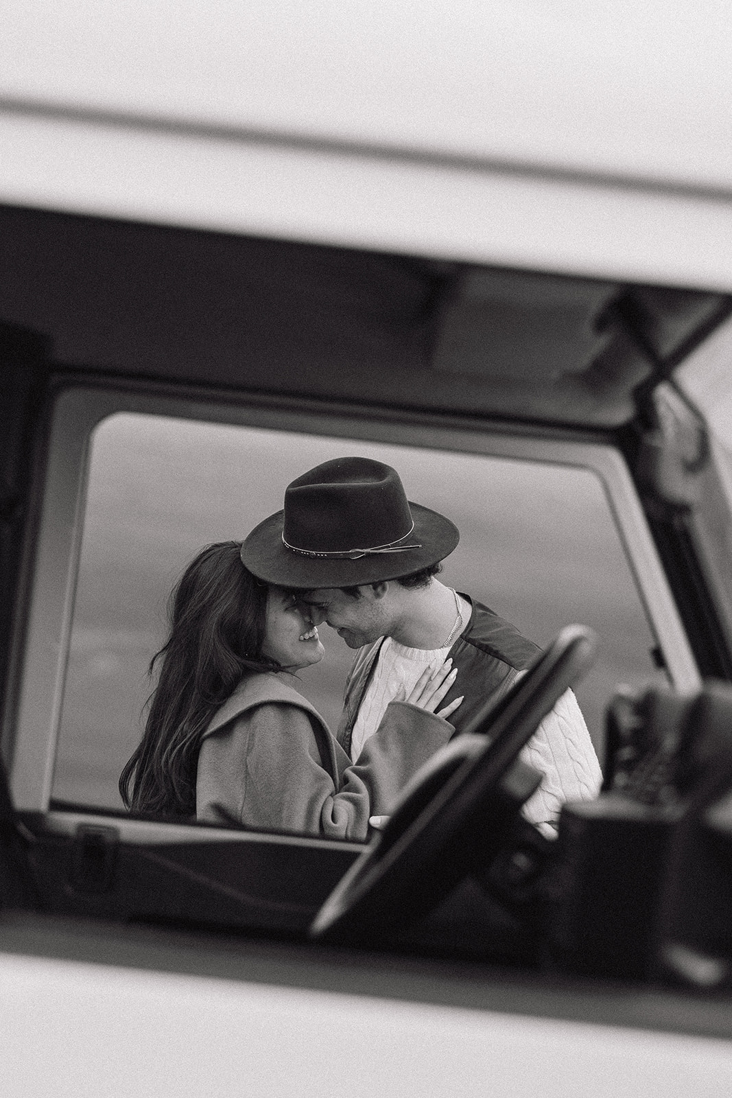 candid photo through the driver seat window of bride and groom leaning in for a kiss