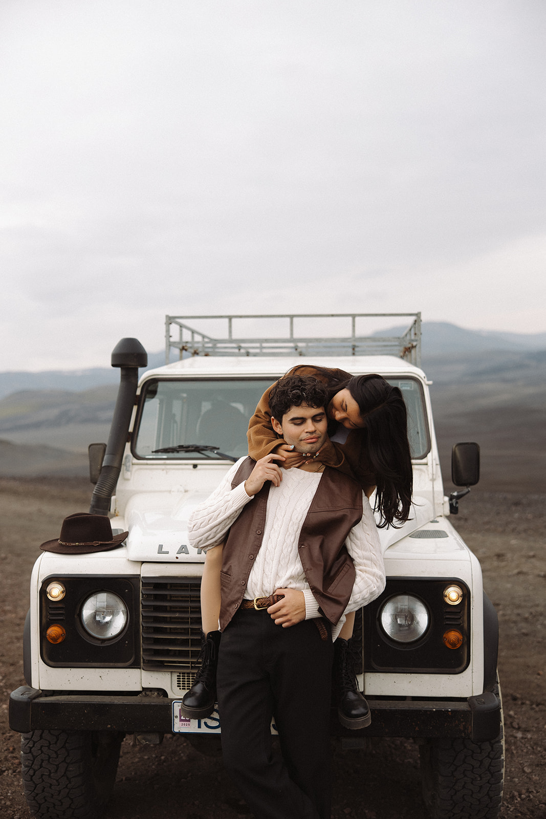 bride leans over to kiss the groom while sitting on a while 4x4 in iceland