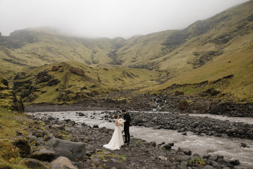 bride and groom pose for portraits in iceland surrounded by mountains, creek, and rocky terrain