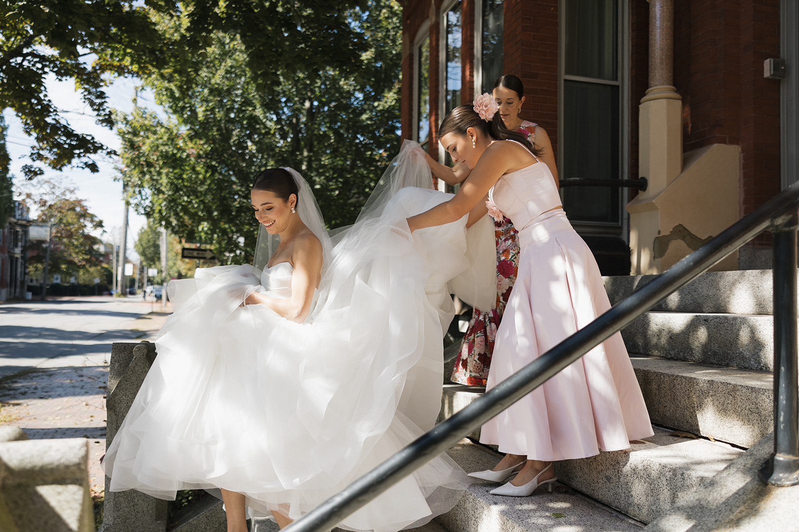bride is helped down the stairs with her mom and sister before their dreamy Portland, Maine courthouse wedding 