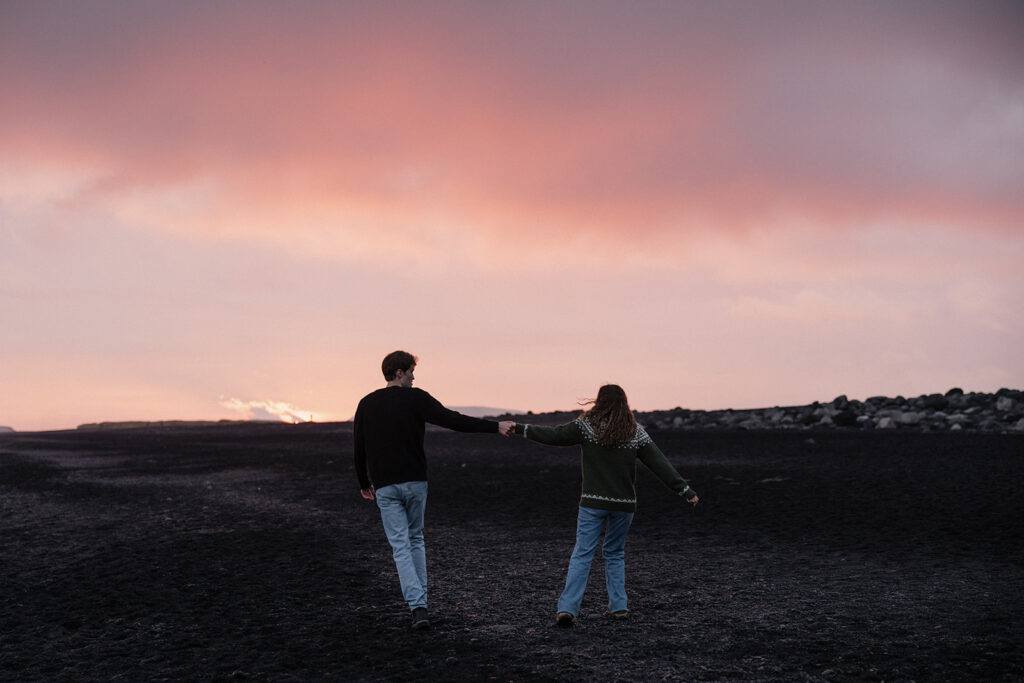 Couple walks along a rocky beach with a gorgeous pink and purple sunset in Iceland 