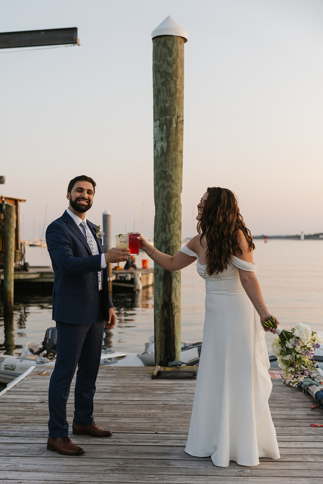 bride and groom share a drink together on the dock