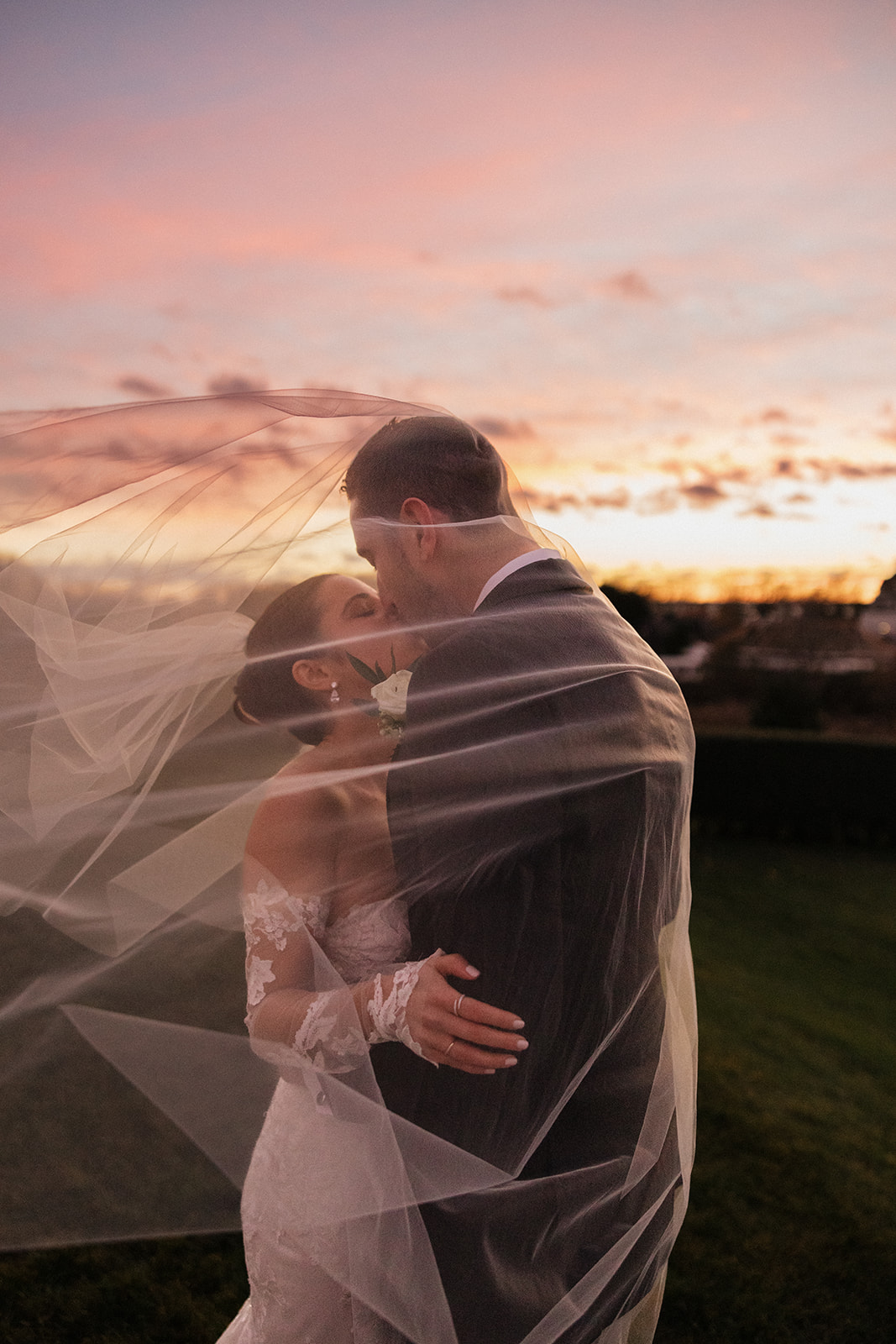 bride and groom share a kiss covered by her veil with the stunning New Hampshire sunset behind them