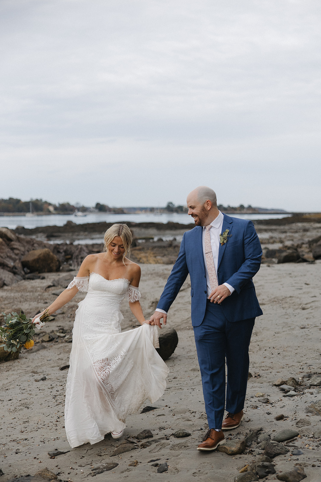 bride and groom walk on the New Hampshire coast together laughing and enjoying their beautiful wedding day