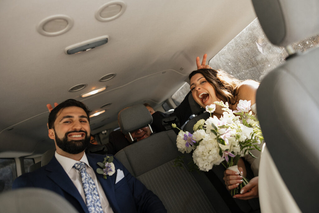 bride and groom ride in the limo on their wedding day as their wedding party gives them bunny ears from the back