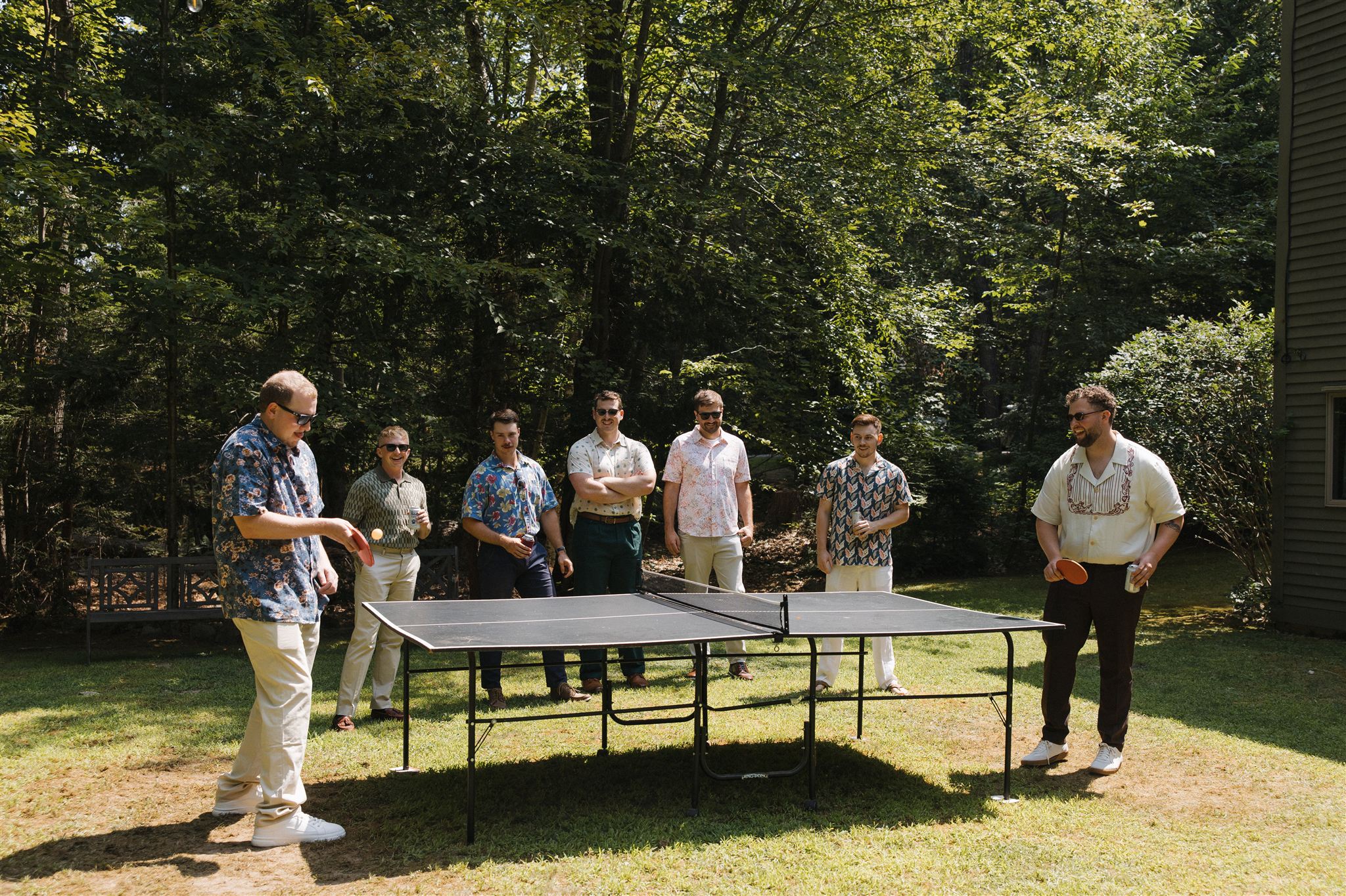 groomsmen play ping pong together as they prepare for the Maine wedding day