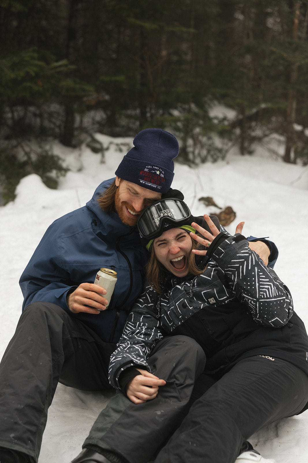 bride shows off her ring as the couple sit together on the snow during the surprise ski proposal