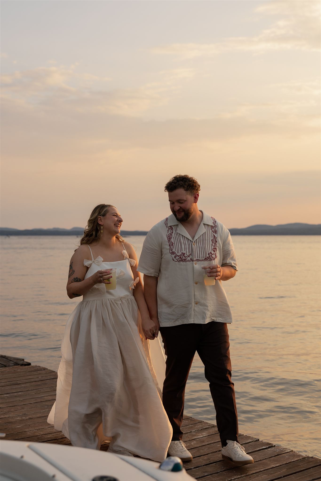 bride and groom walk on the dock together sharing laughs and drinks