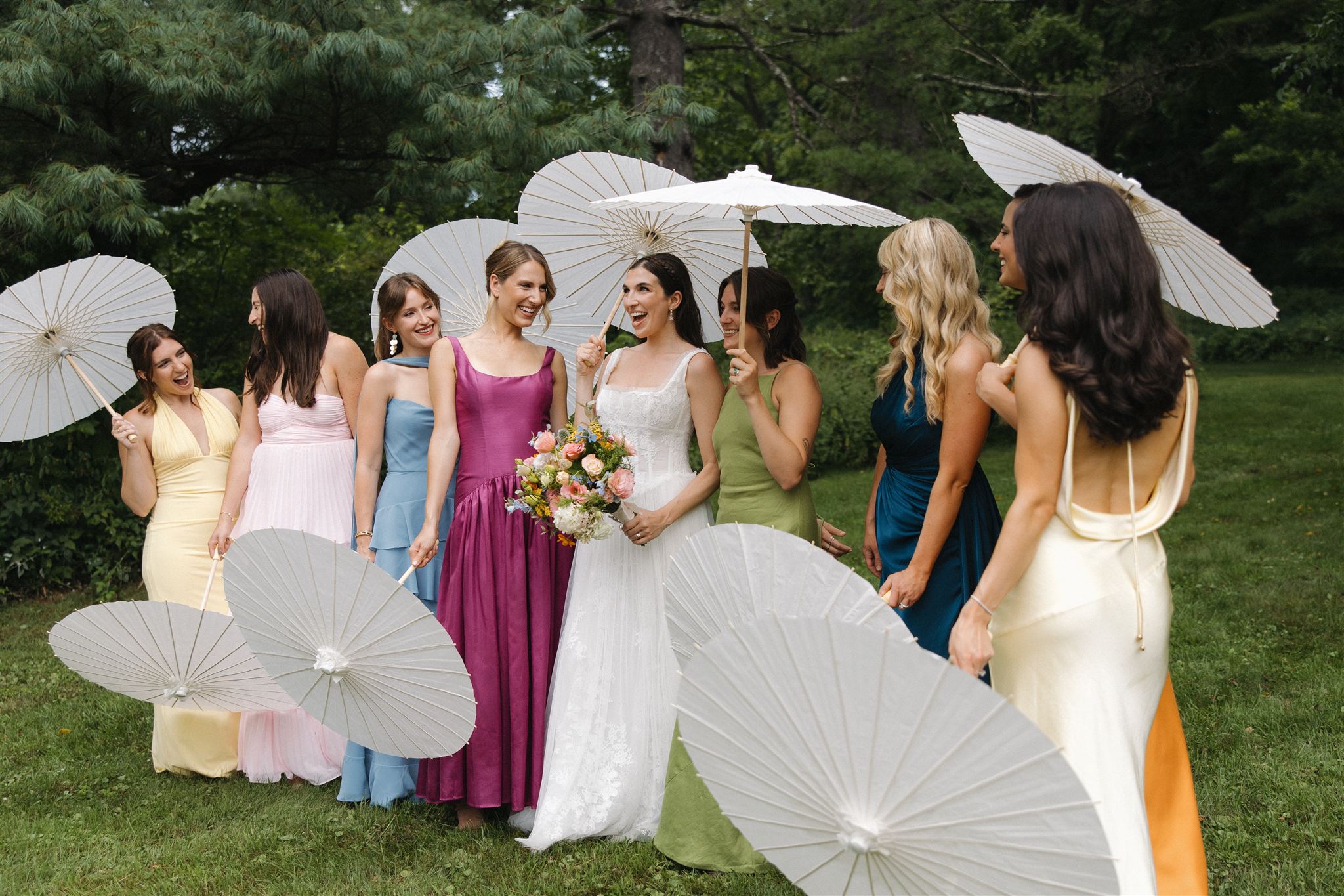 beautiful wedding party poses for a photo with their all white umbrellas