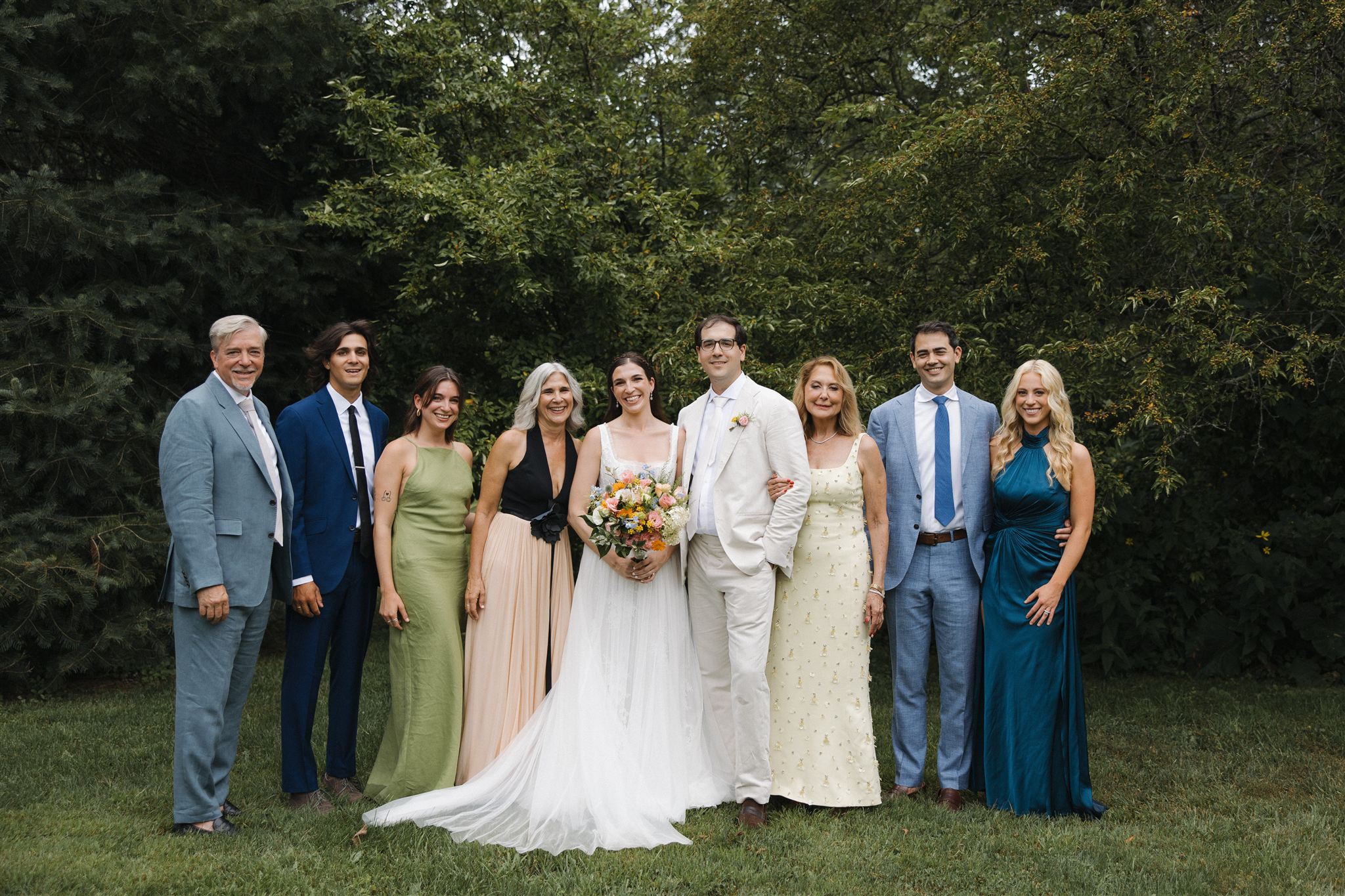 bride and groom pose for a photo with their families with the forrest as a backdrop 