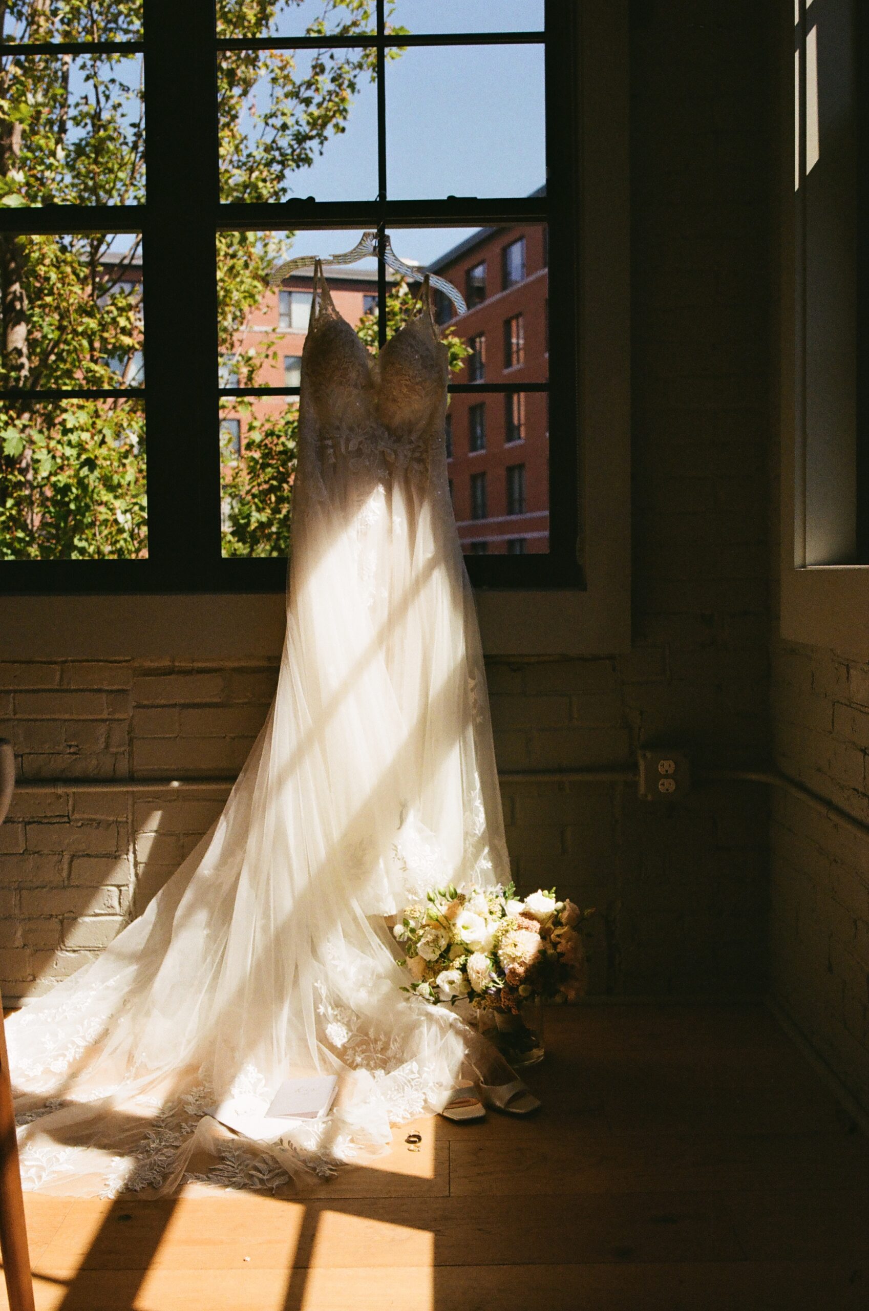 brides wedding dress hangs in the window waiting for the final prep