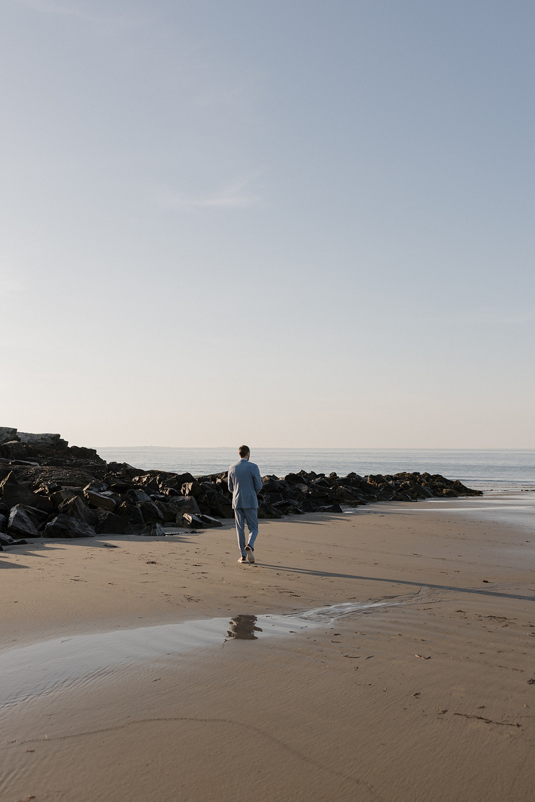 groom walks on the New Hampshire beach after his elopement