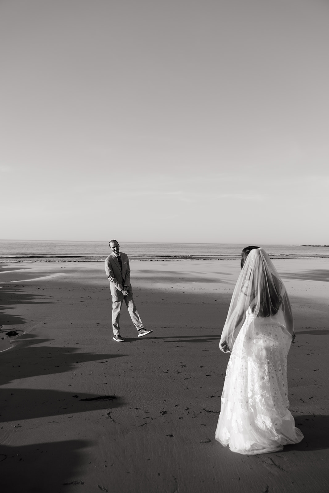 bride and groom share candid romantic moments during their first look session on the New Hampshire beach