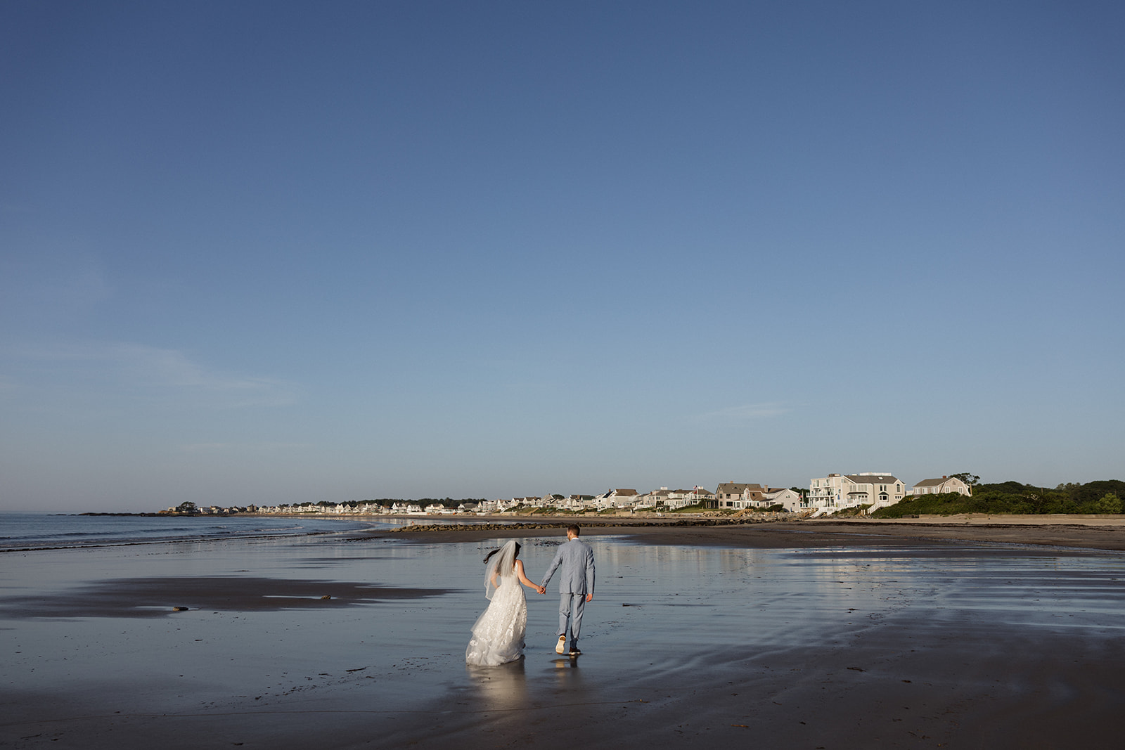 bride and groom walk on the beach togedther