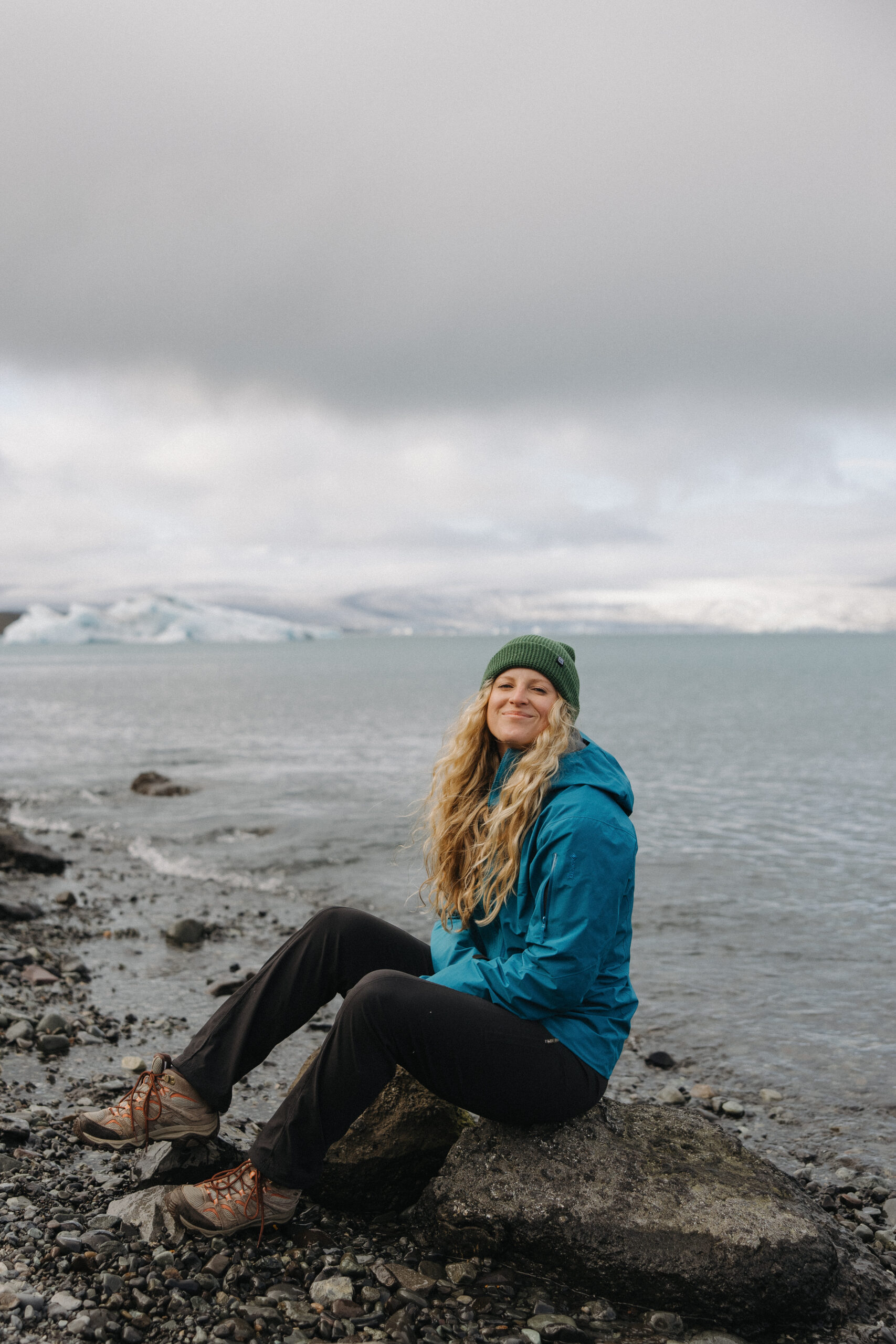 Erica sits on a rock with the coastline stretching behind her
