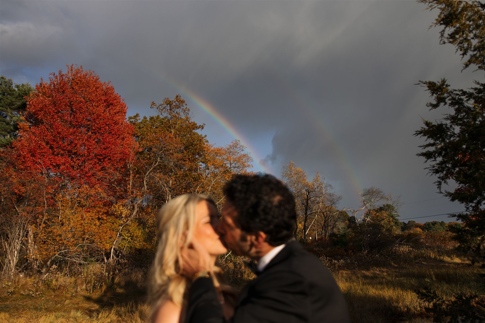 bride and groom share a laugh as a rainbow stretches over their heads