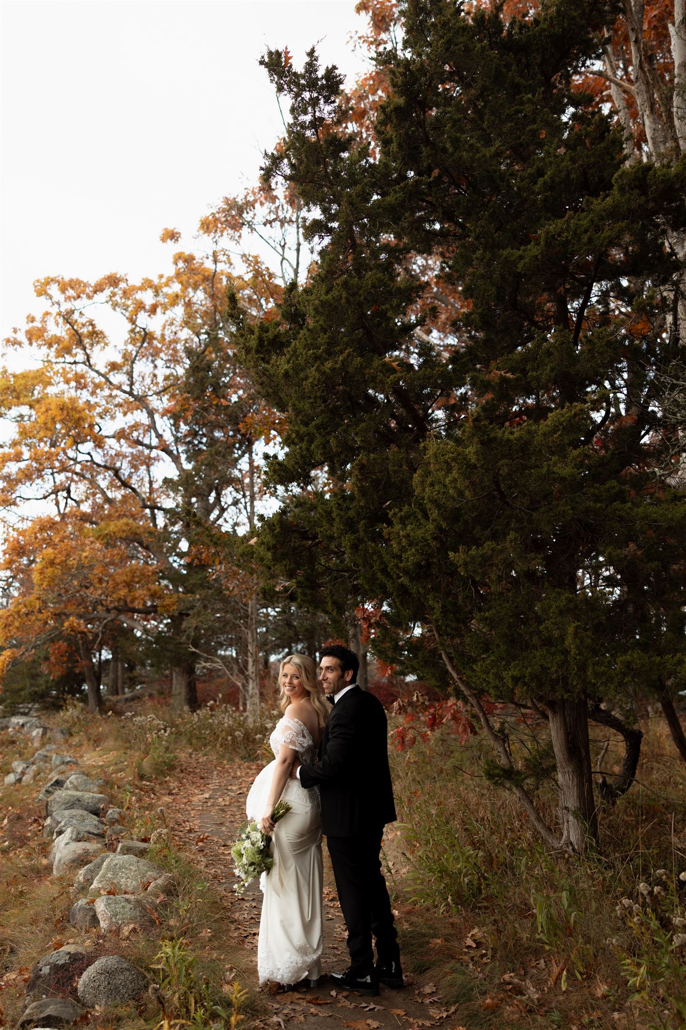 bride and groom stop and pose under the fall foliage during their Seacoast post wedding photoshoot