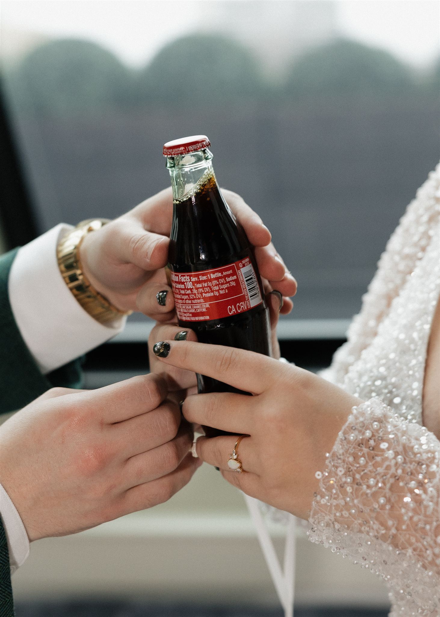 bride and groom hold a coke bottle together as they start to open each one