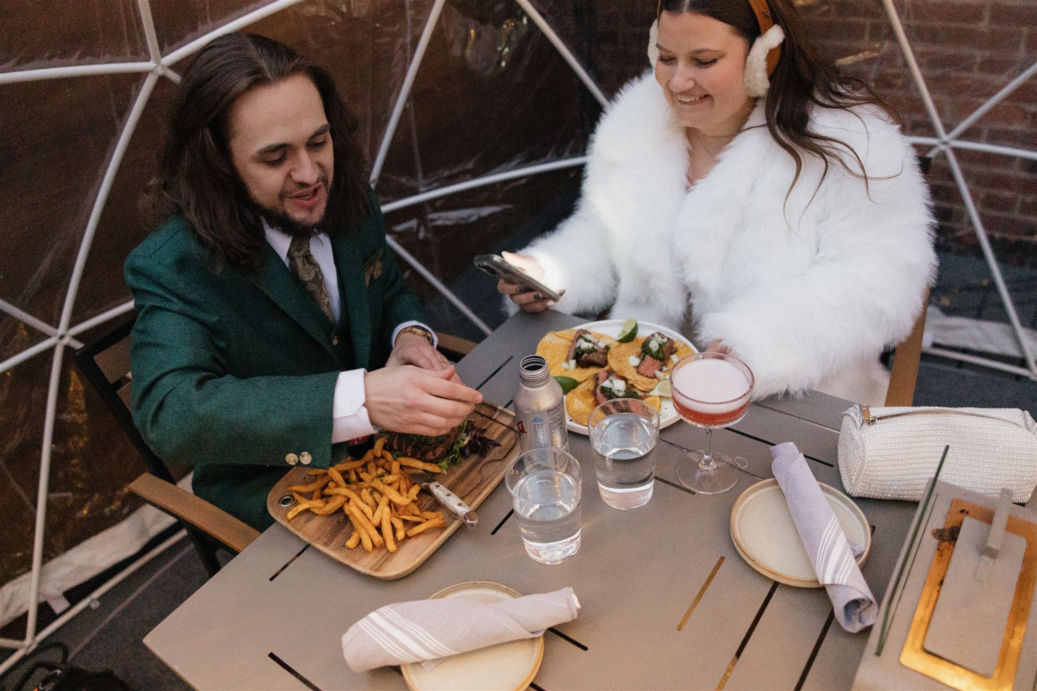 bride and groom eat a romantic dinner together in  rooftop igloo