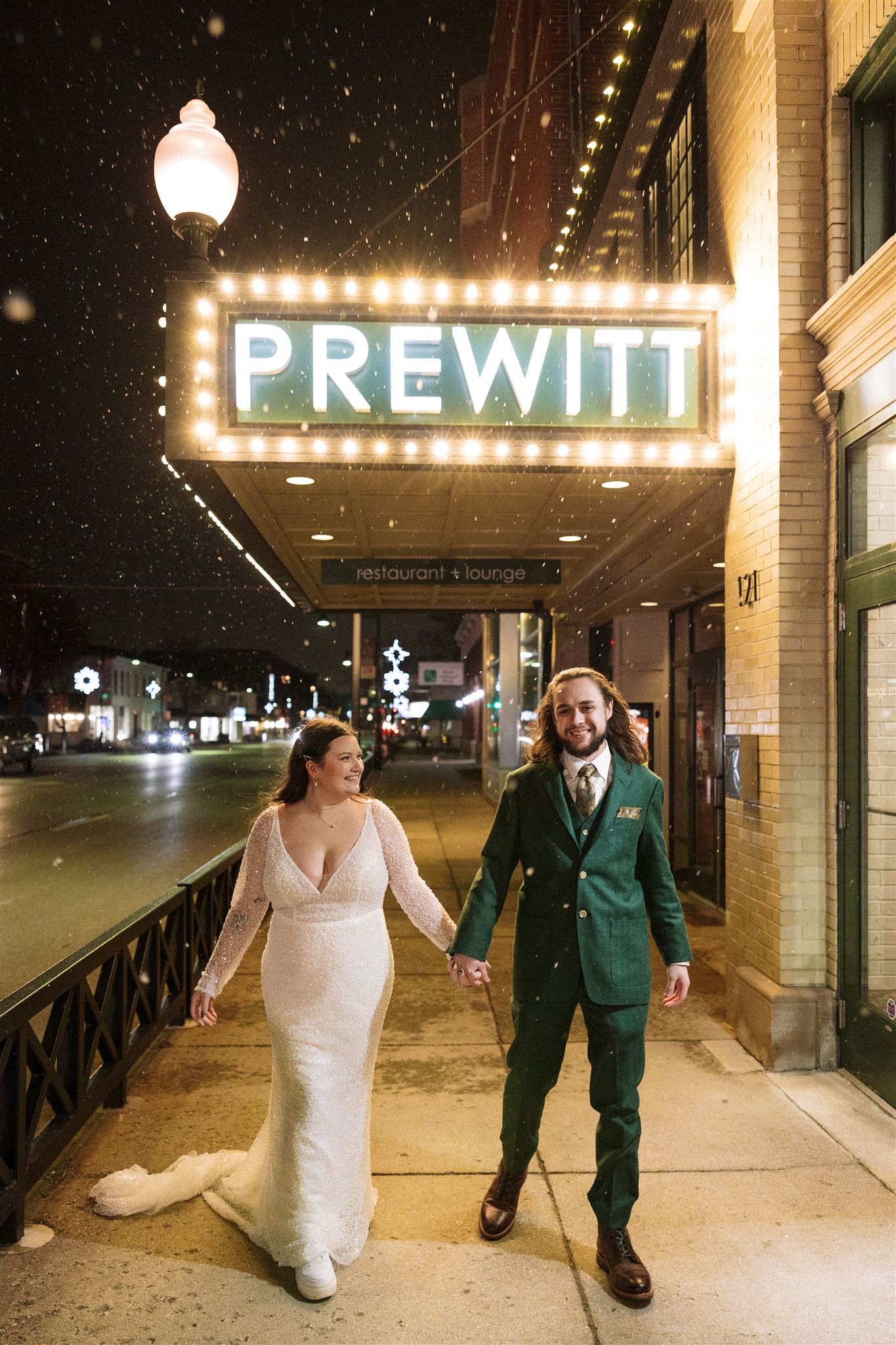 bride and groom walk on the streets as snow begins to fall