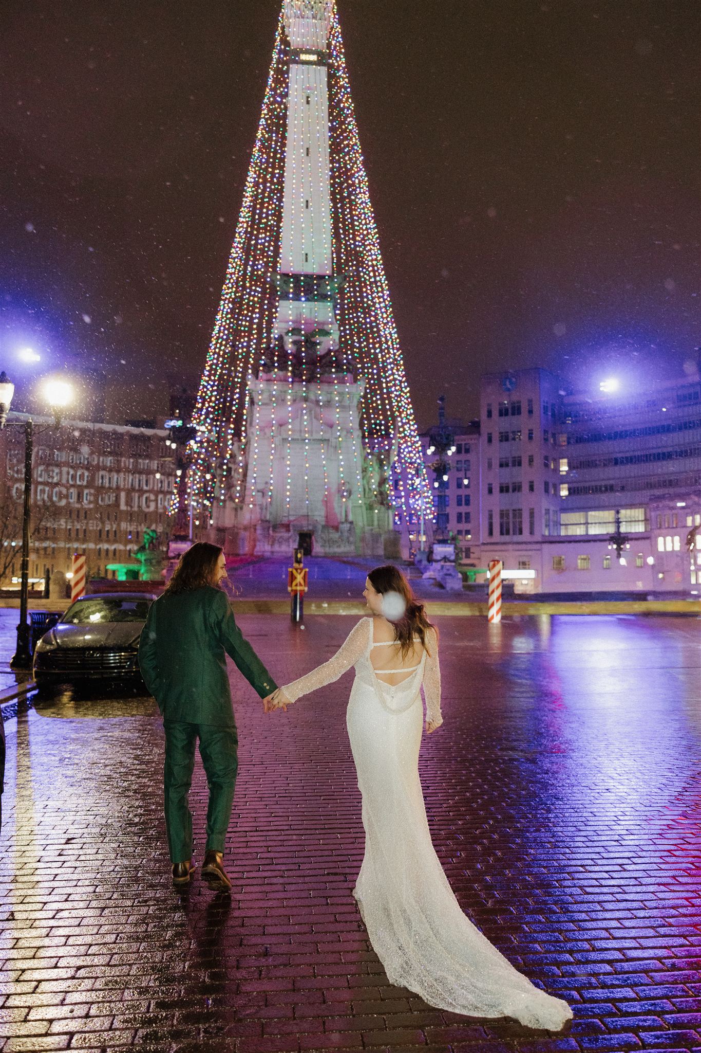 bride and groom walk toward monument circle as the snow begins to fall