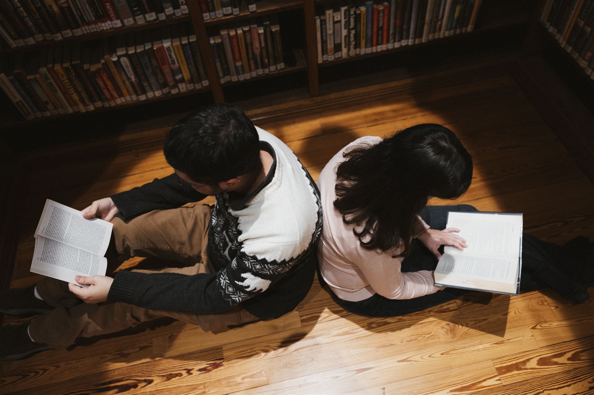 couple pose back to back reading books during their library engagement photos