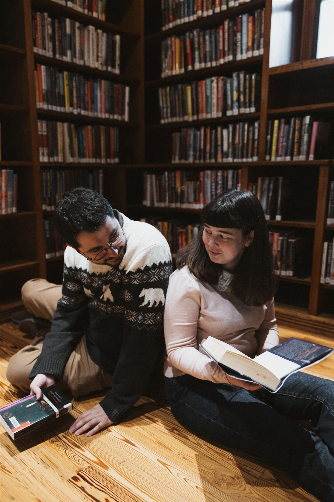 couple pose back to back reading books during their library engagement photos