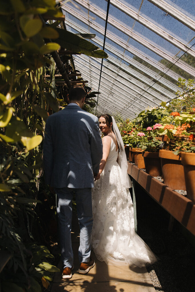 Couple walking through the greenhouse at Fuller Gardens after saying their vows in the courtyard. 