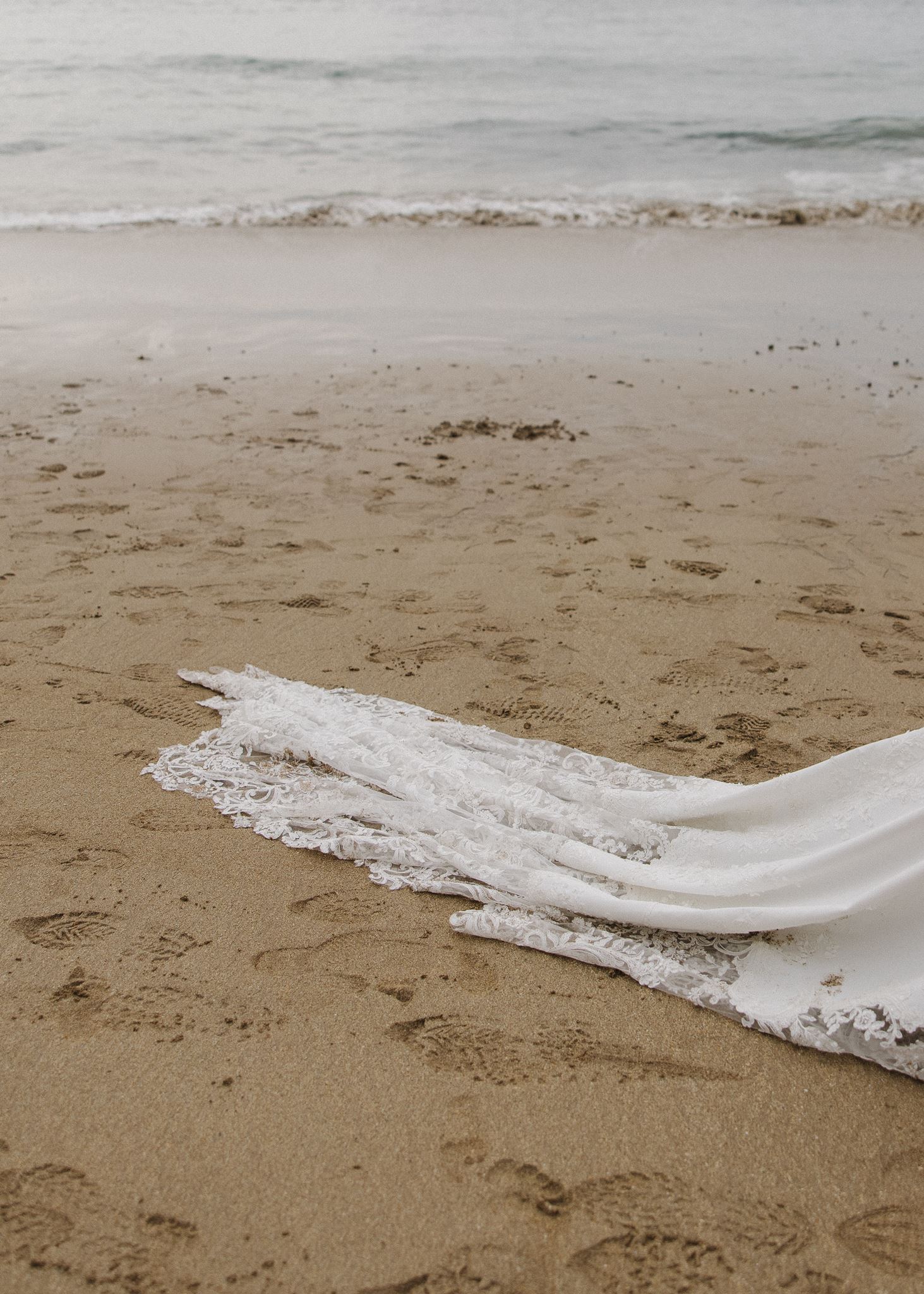brides dress drags in the sand as they walk on the beach