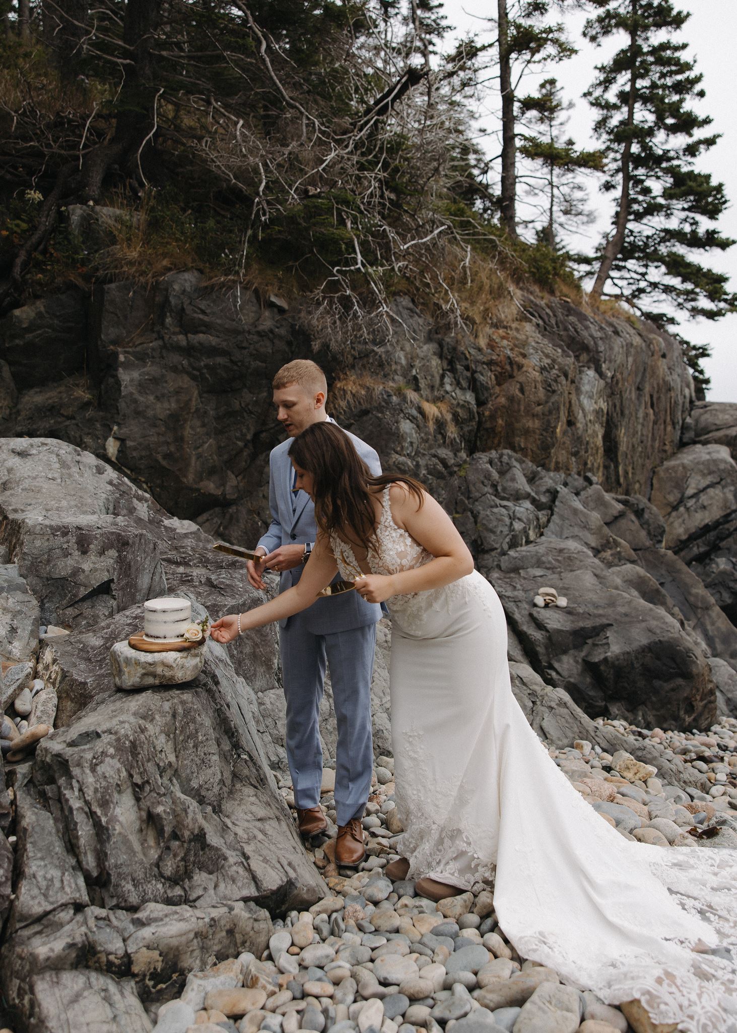 bride and groom start the cake ceremony while the cake rests on a rock
