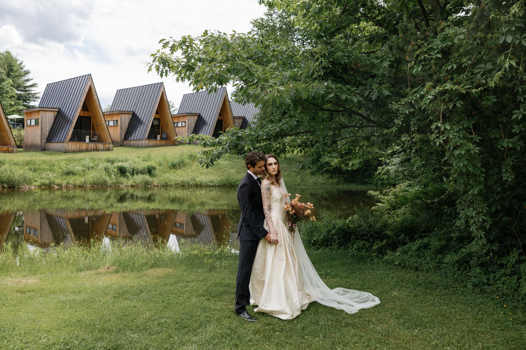 bride and groom pose in front of the A frame cabins and pond