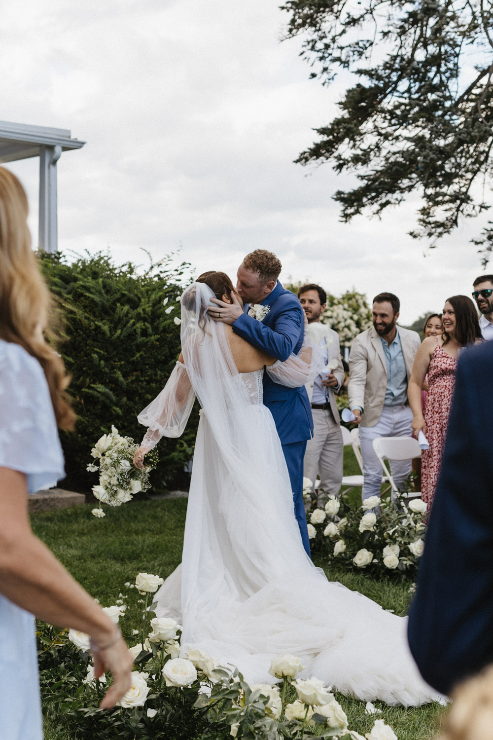 bride and groom share a kiss as their guests celebrate 